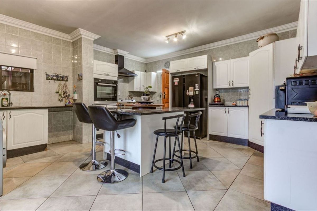 Spacious kitchen featuring a central island with breakfast bar seating, granite countertops, built-in oven, and ample cabinetry with a tiled splashback.