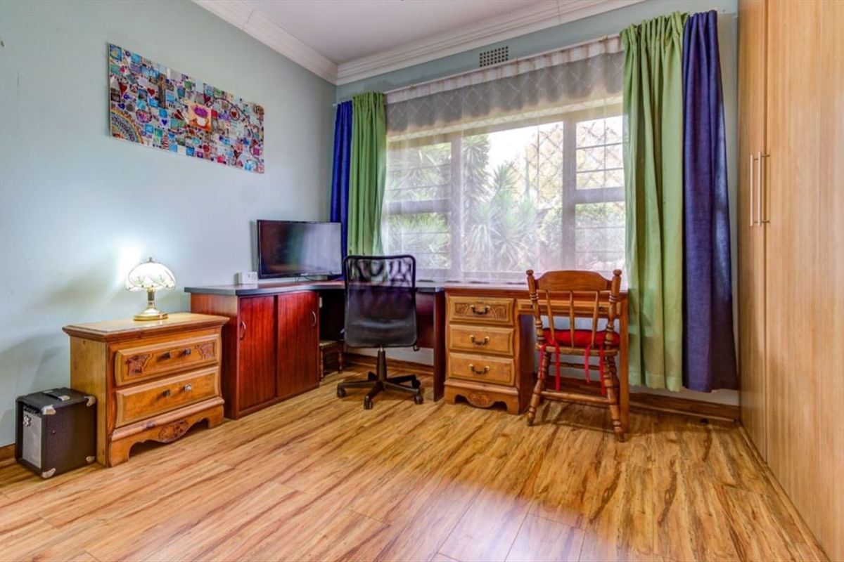 A bedroom featuring laminate flooring, a built-in wardrobe, and a large window with security bars, currently utilized as a home office space.