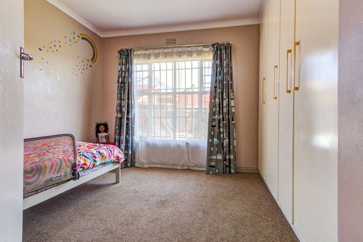 A bedroom featuring built-in wardrobes, carpeted flooring, and a window with security bars, providing a functional and well-lit living space.