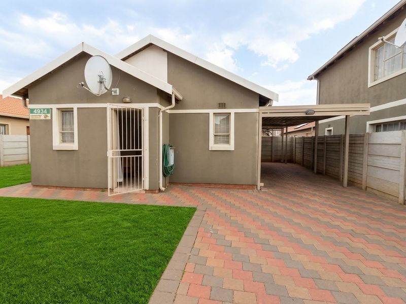 Front view of a residential property featuring a paved driveway, attached carport, security gate, and a well-maintained lawn area.