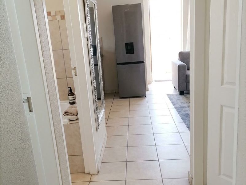 A tiled hallway providing access to adjacent rooms, including a bathroom and a living area with natural light.