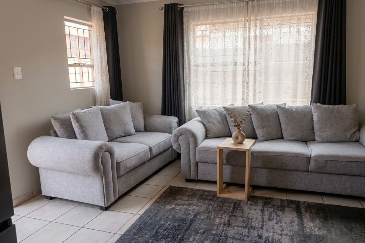 A comfortable living room featuring neutral tiled flooring, large windows with security bars, and modern curtain fixtures, creating a bright and inviting space.