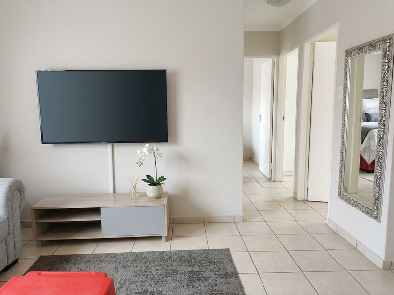 A bright living area featuring neutral tiled flooring and access to multiple internal rooms through standard doorways.