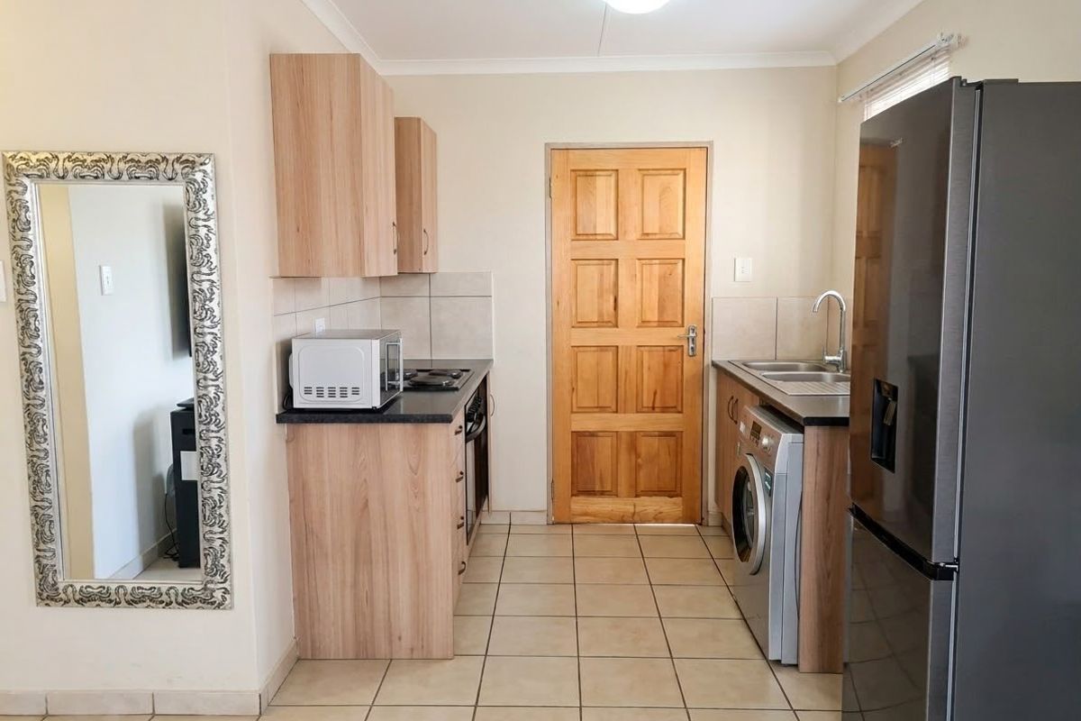 A functional kitchen featuring light wood-tone cabinetry, dark countertops, tiled flooring, and integrated appliance spaces, providing a clean and practical culinary area.