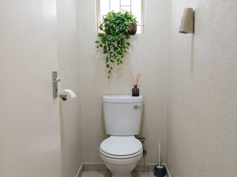 A compact, well-maintained guest bathroom featuring a standard toilet, tiled flooring, and a small window with security bars.