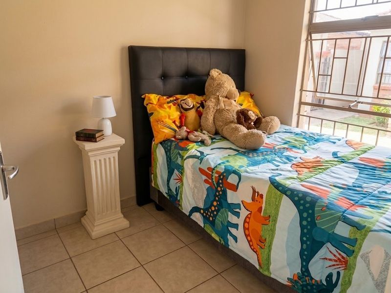 A bedroom featuring tiled flooring and a window fitted with security bars, providing natural light and ventilation.