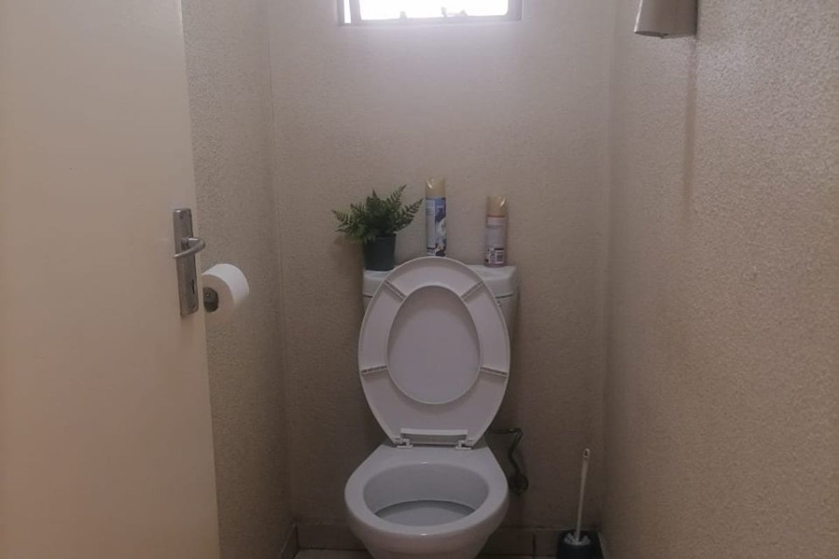 A compact guest toilet featuring a standard white toilet suite, tiled flooring, and a small window with security bars.