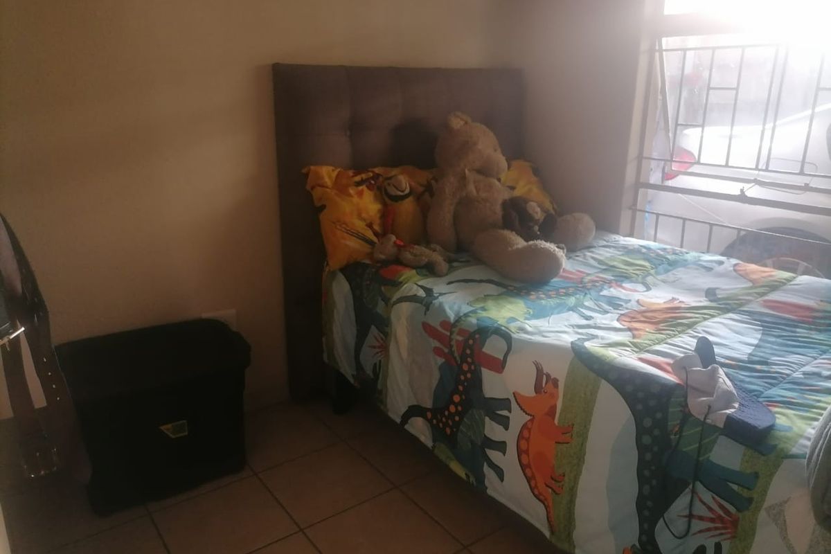 A bedroom featuring tiled flooring and a window with security bars, providing a functional space for a child's room.