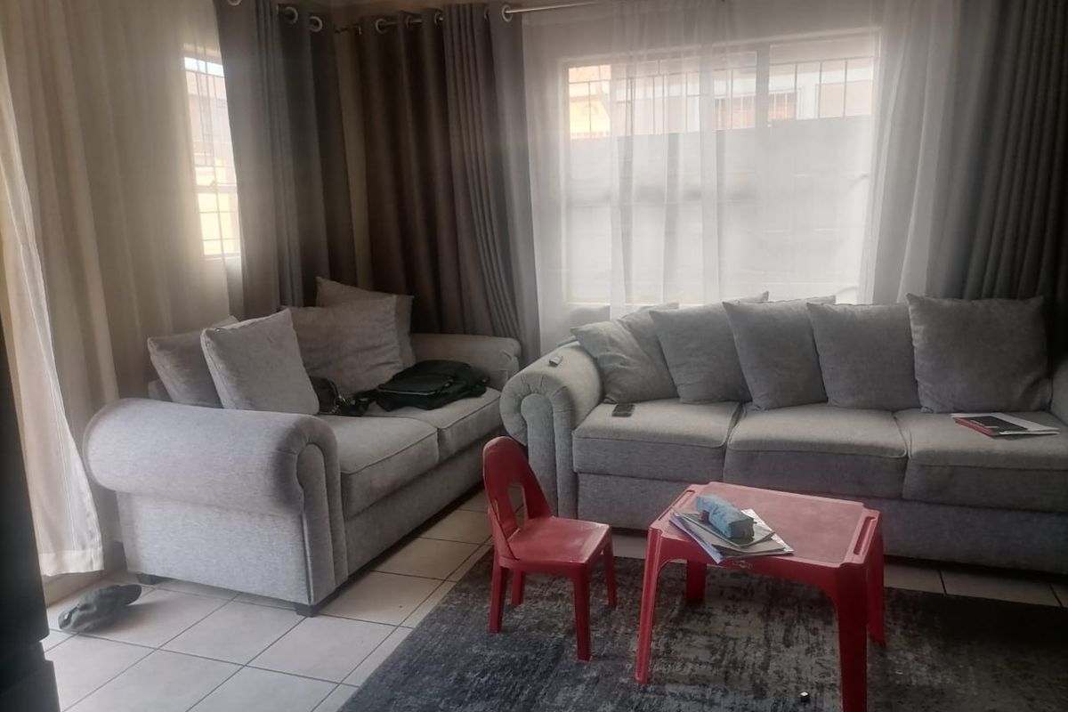 A comfortable living room featuring tiled flooring and large windows with curtain treatments, providing a bright and functional space for relaxation.