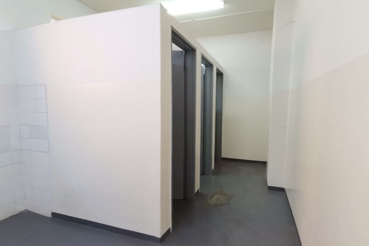 A functional industrial restroom facility featuring multiple partitioned cubicles with painted walls and durable flooring.