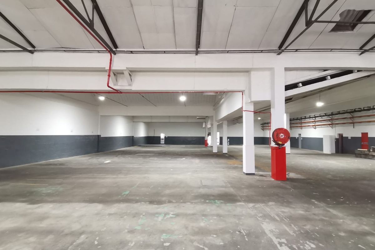 Spacious industrial warehouse area featuring high ceilings, exposed structural beams, fire safety equipment, and durable concrete flooring suitable for various commercial or storage operations.