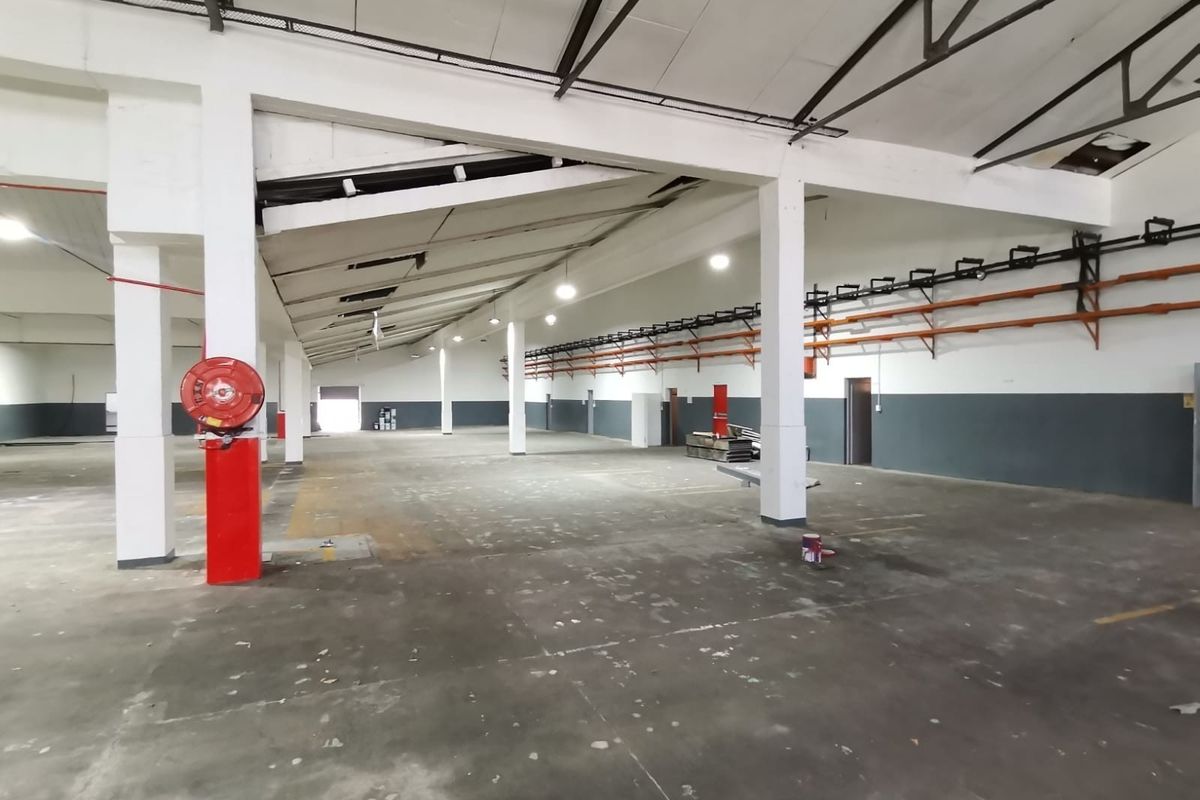 Spacious industrial warehouse featuring high ceilings, exposed structural beams, concrete flooring, and wall-mounted fire safety equipment.
