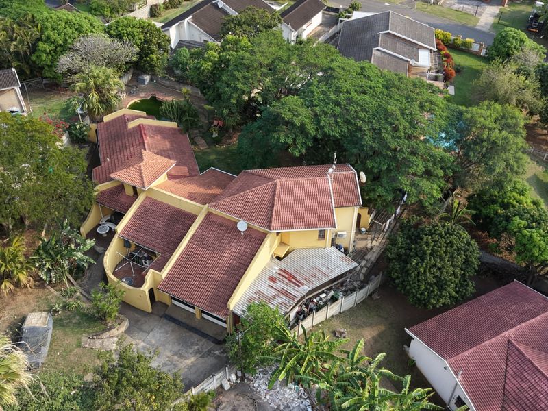 Aerial view of a residential property featuring a multi-pitched tiled roof, established garden, and a covered patio area.