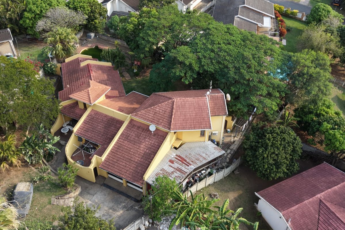 Aerial view of a residential property featuring a multi-pitched tiled roof, established garden, and a covered patio area.