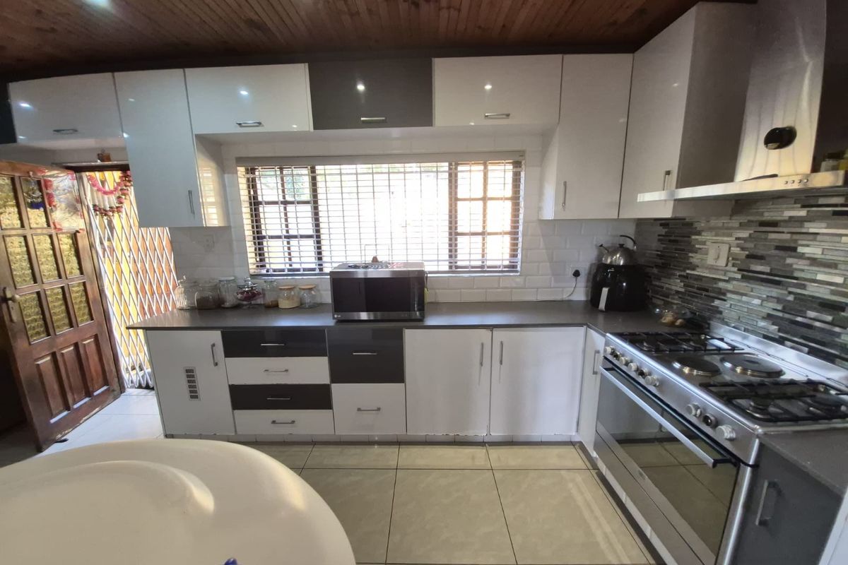Modern kitchen featuring high-gloss cabinetry, subway tile backsplash, stainless steel gas stove with extractor fan, and tiled flooring.