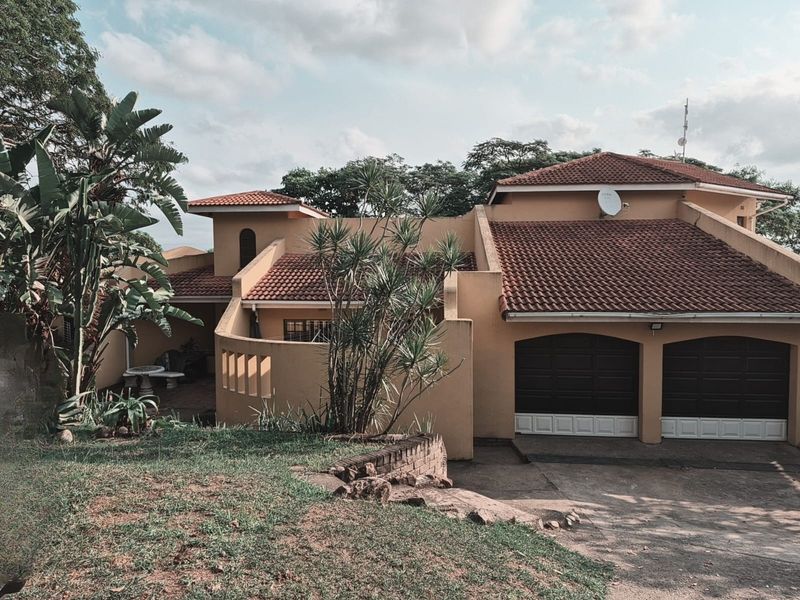 Exterior view of a multi-level residential property featuring a double garage, terracotta tiled roof, and a paved driveway with surrounding garden area.