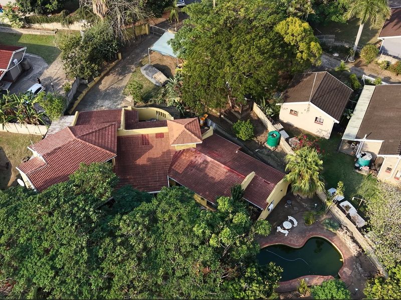 Aerial view of the property featuring a tiled roof, private swimming pool, and surrounding garden area within a residential neighborhood.