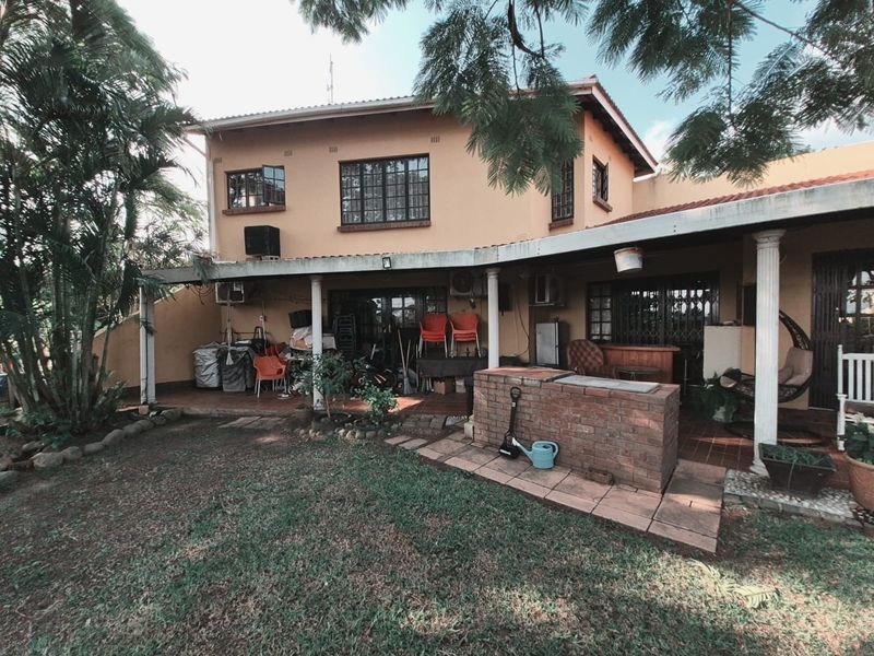 Rear view of a two-story house featuring a covered patio area with a built-in brick braai and garden access.