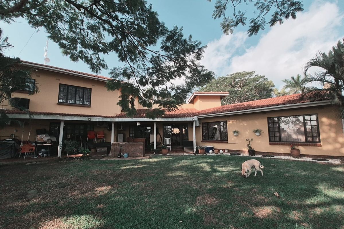 Spacious rear exterior view of the house featuring a covered patio area, terracotta roof tiles, and a large established garden.