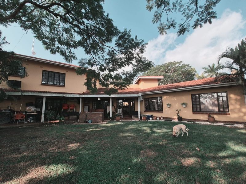 Spacious rear exterior view of the house featuring a covered patio area, terracotta roof tiles, and a large established garden.