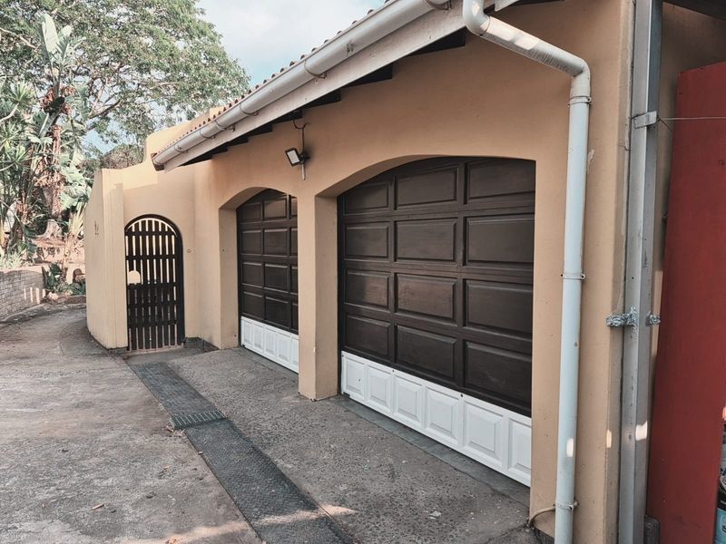 A double garage featuring dark brown paneled doors with white lower sections, complemented by a side pedestrian gate and exterior security lighting.