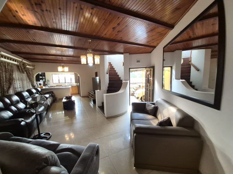Spacious open-plan living area featuring a vaulted timber-clad ceiling, tiled flooring, and a central staircase leading to the upper level.