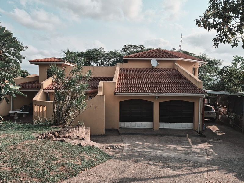 Front elevation of a double-story residential house featuring a double garage, tiled roof, and paved driveway with established garden surroundings.