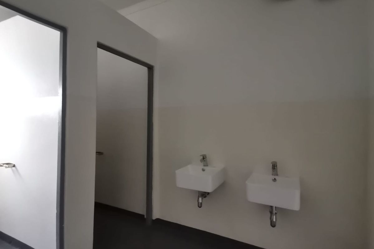 A clean, functional industrial restroom facility featuring two wall-mounted ceramic washbasins and separate cubicle access points.