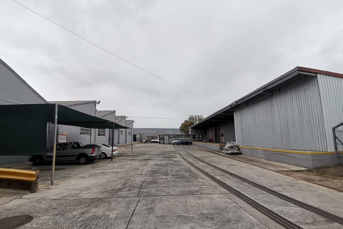 Industrial yard area featuring concrete paving, loading bays, and metal-clad warehouse structures with integrated rail tracks.