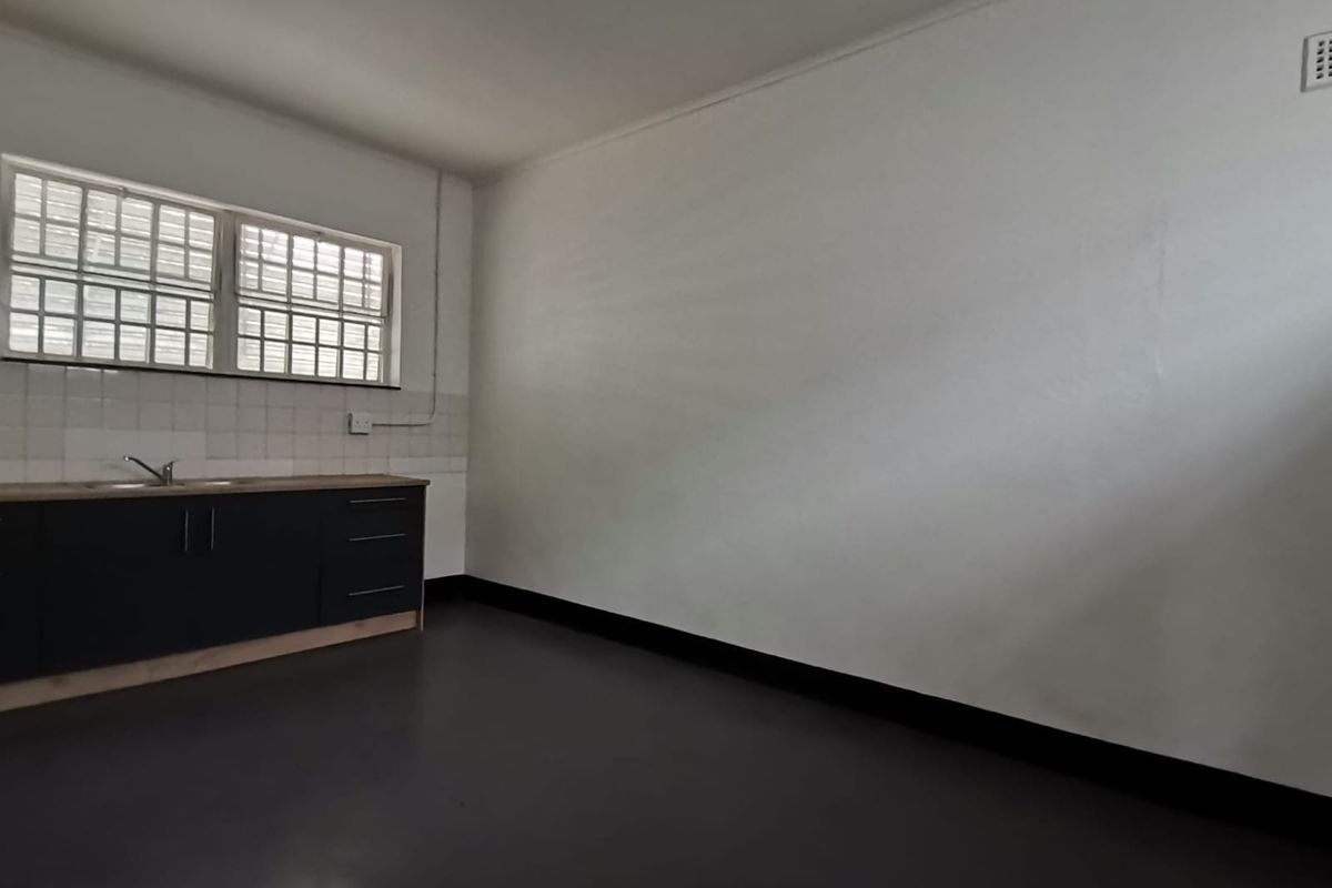 A functional kitchenette area featuring dark cabinetry, a stainless steel sink, and a window with security bars.