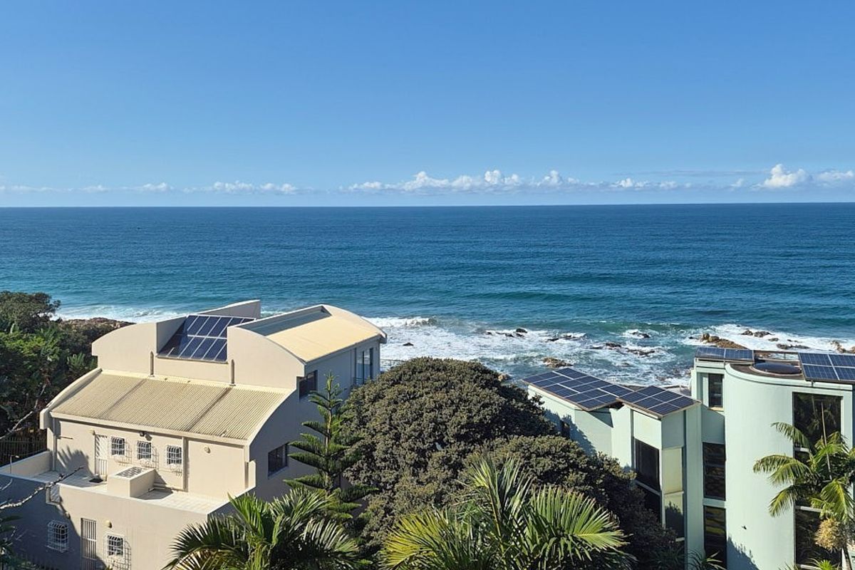 An elevated aerial view showcasing the property's coastal location, featuring solar panel installations on the roof structures overlooking the ocean.