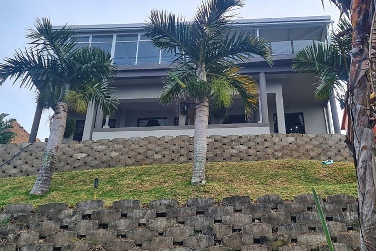 A rear view of a multi-level house featuring tiered retaining walls, landscaped garden, and a spacious covered balcony on the upper level.