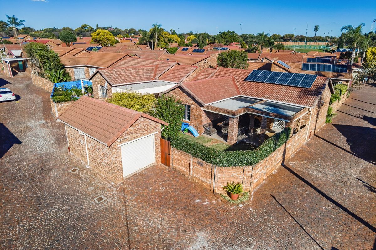 Aerial view of a brick townhouse featuring a tiled roof, solar panels, a private garage, and a covered patio area within a residential complex.