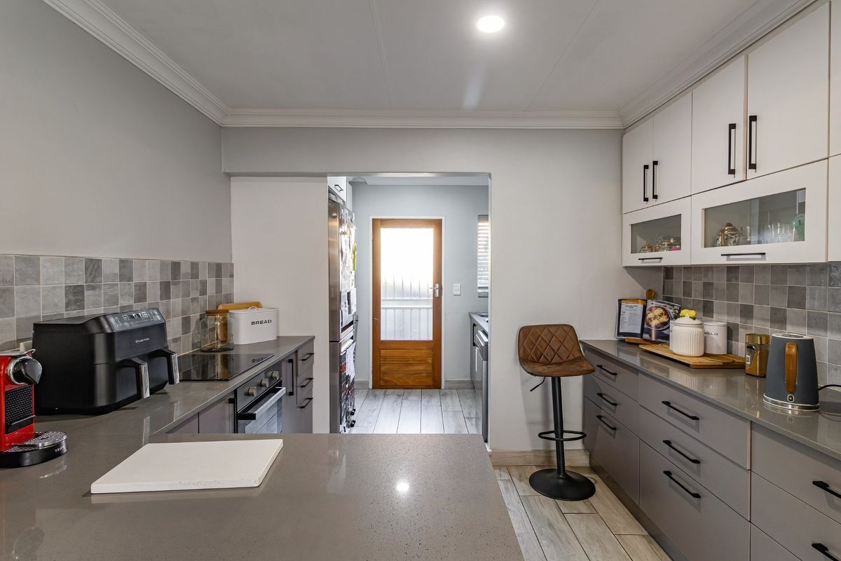 Modern kitchen featuring grey cabinetry, stone countertops, tiled backsplash, and integrated oven and hob, with an adjacent scullery area.