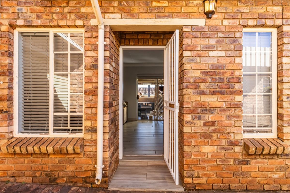 Exterior view of a townhouse entrance featuring face-brick facade, security gate, and tiled threshold leading into the interior living space.