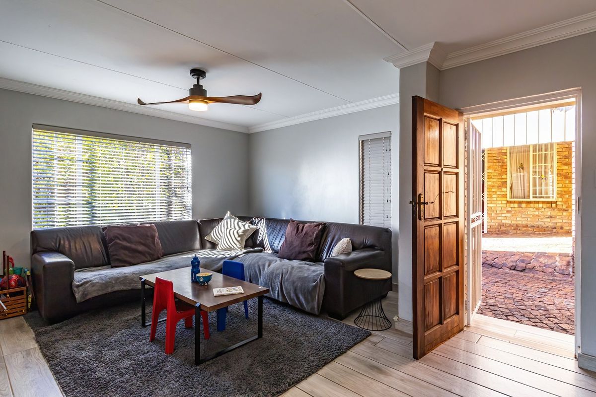 A comfortable living room featuring light-toned wood-look flooring, crown molding, a modern ceiling fan, and direct access to an outdoor paved area.