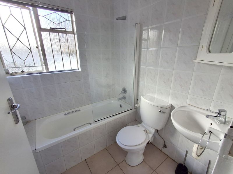 A functional bathroom featuring a bathtub with a glass screen, pedestal basin, and toilet, finished with neutral wall and floor tiles.