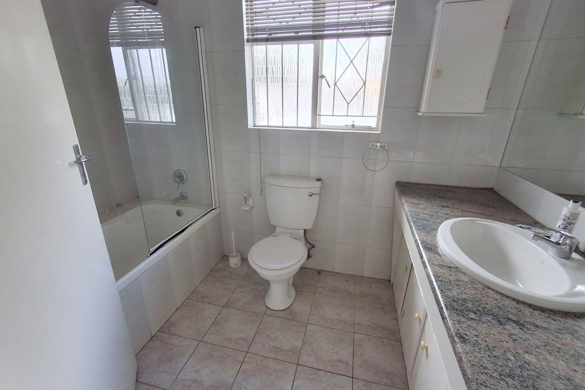 A functional bathroom featuring a built-in vanity with granite countertop, a bathtub with a glass screen, and tiled finishes throughout.