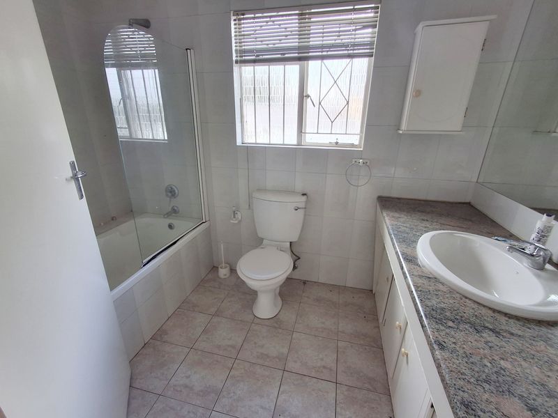 A functional bathroom featuring a built-in vanity with granite countertop, a bathtub with a glass screen, and tiled finishes throughout.
