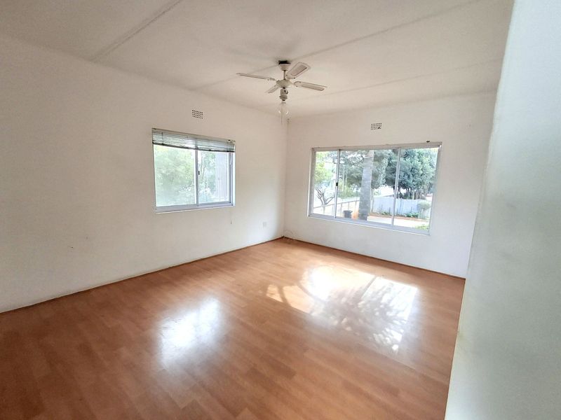 A bright, empty office space featuring laminate flooring, a ceiling fan, and large windows providing natural light.