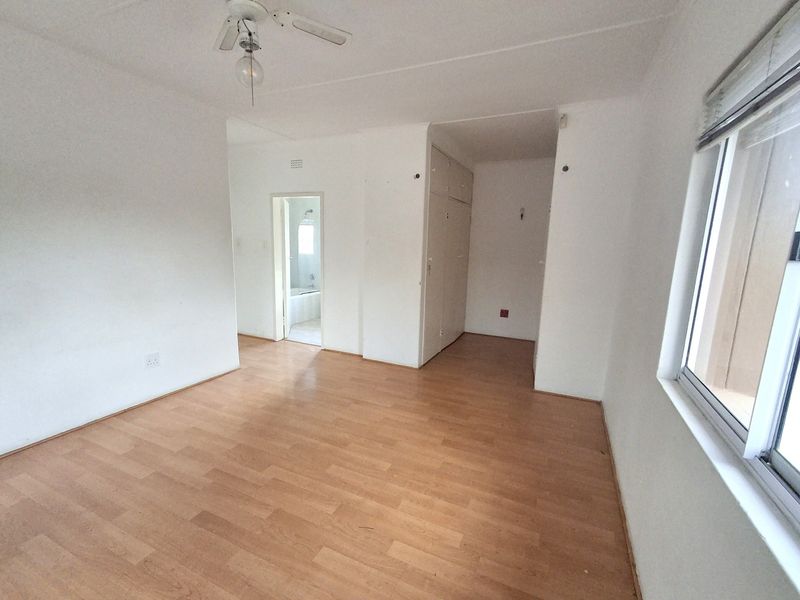 An empty bedroom featuring laminate flooring, built-in cupboards, and a ceiling fan, with an adjoining bathroom visible through the doorway.