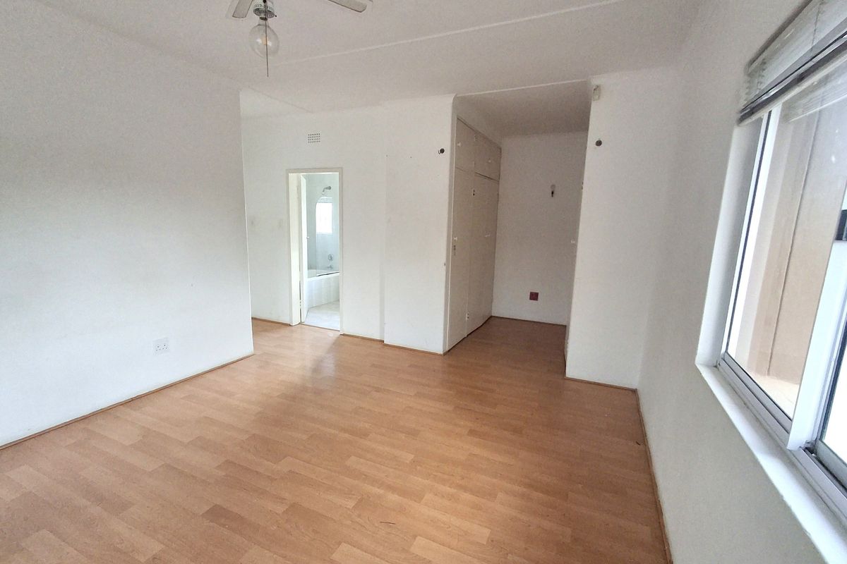An empty bedroom featuring laminate flooring, built-in cupboards, and a ceiling fan, with an adjoining bathroom visible through the doorway.