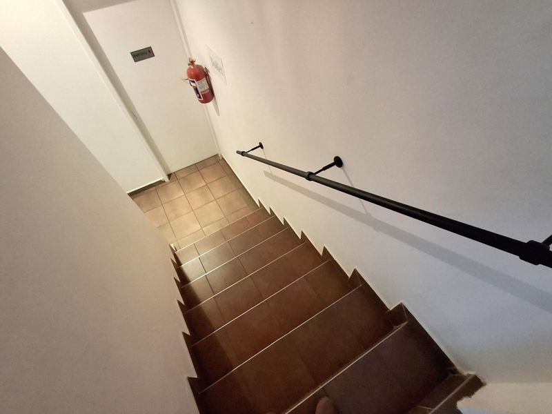 A functional office stairwell featuring tiled steps, a black metal handrail, and a wall-mounted fire extinguisher.