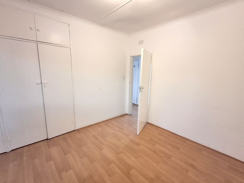 A bright, empty office space featuring light wood-look laminate flooring and ample built-in storage cupboards.