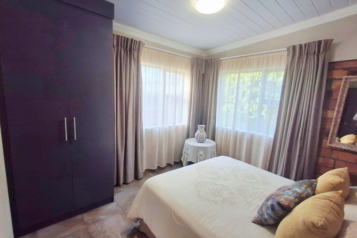 A bedroom featuring a built-in wardrobe, tiled flooring, and a textured brick accent wall, providing a functional and cozy living space.