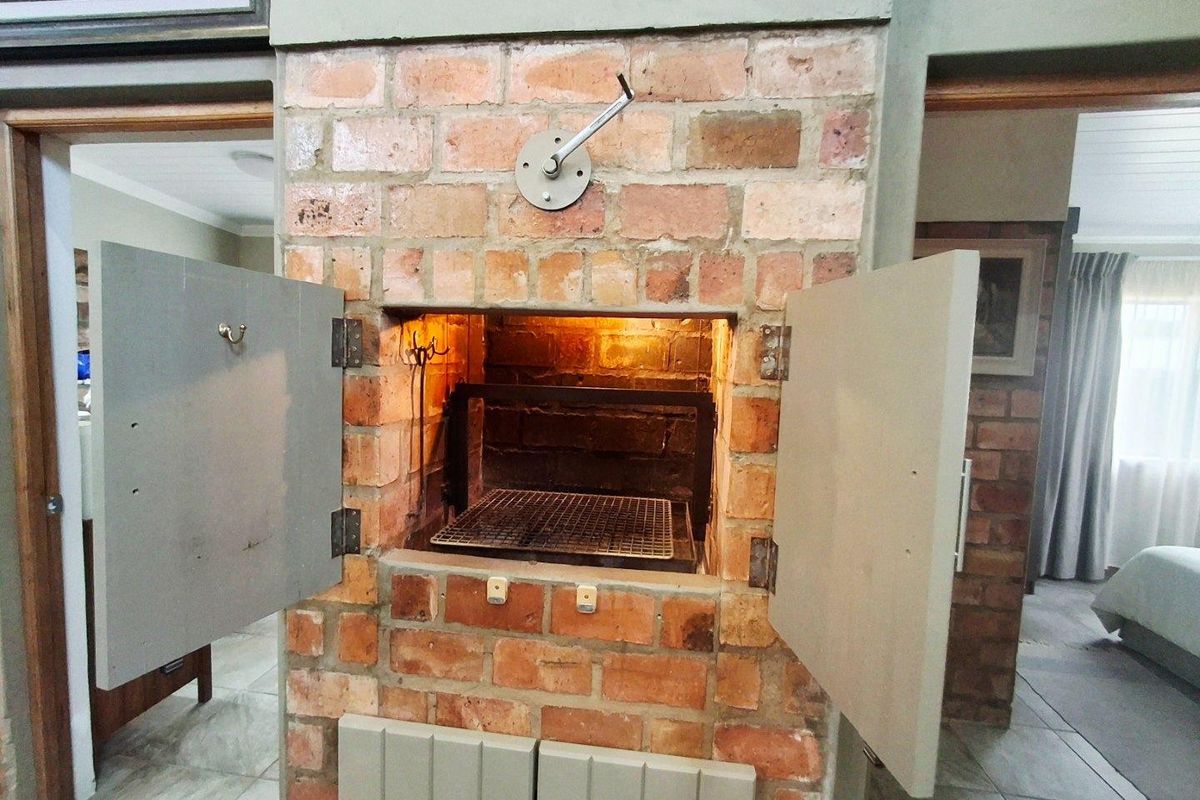 Indoor built-in brick braai or fireplace featuring a metal grill, adjustable height mechanism, and integrated storage cupboards.