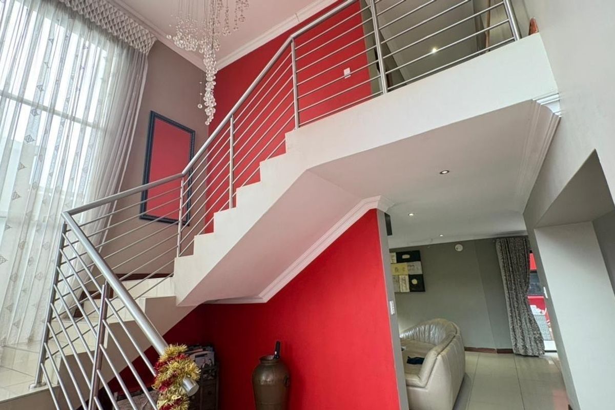A bright double-volume living area featuring a prominent staircase with stainless steel balustrades and modern recessed ceiling lighting.