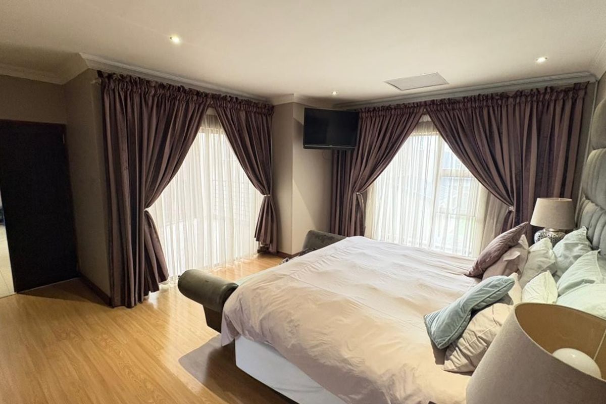 Spacious bedroom featuring laminate flooring, recessed ceiling lighting, and large windows with floor-to-ceiling curtains providing ample natural light.