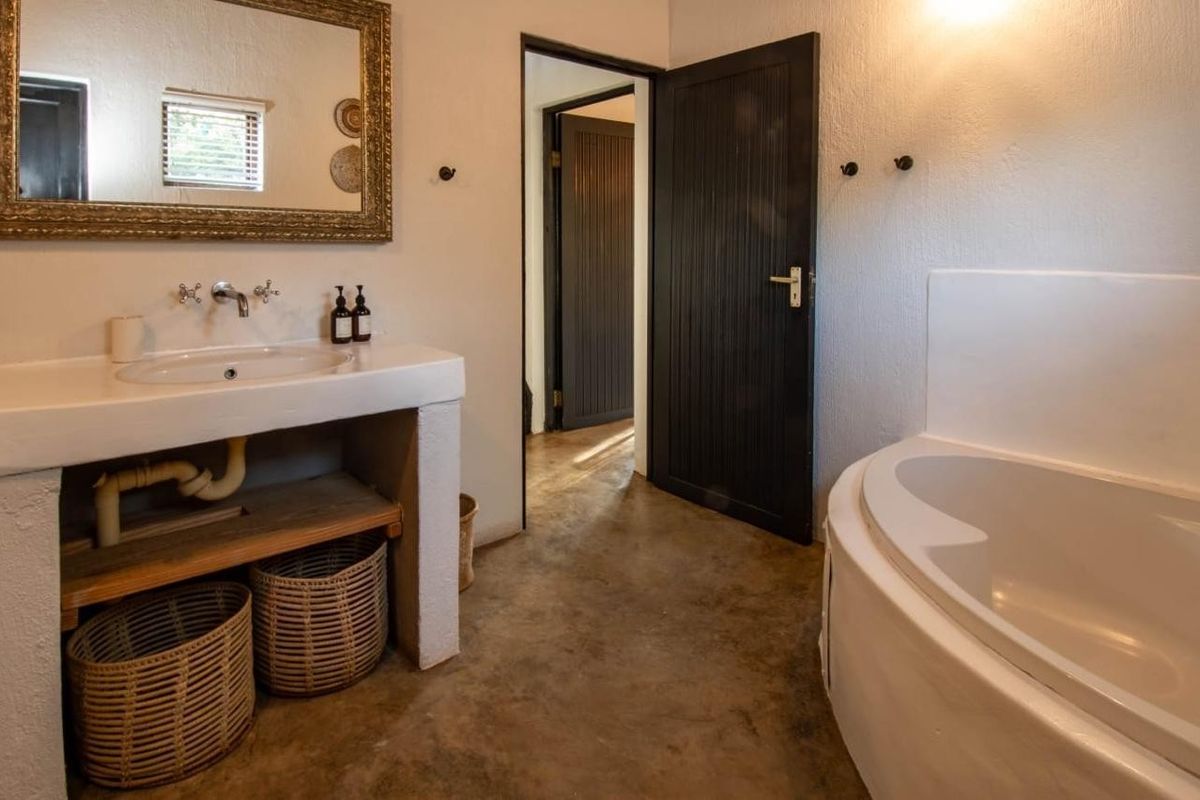 A bathroom featuring a built-in vanity with a drop-in basin, a corner bathtub, and dark-toned interior doors with a rustic concrete floor finish.