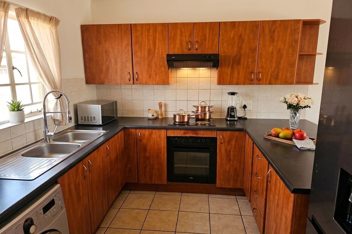 A functional U-shaped kitchen featuring wood-look cabinetry, dark countertops, built-in oven, hob, extractor fan, and tiled flooring with ample storage space.